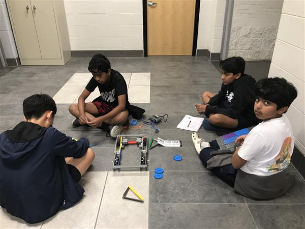 A group of four students sit with their robot at practice.